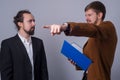 Portrait of two young business people. The boss, holding a folder with documents in his hand, shows with his hand to the side,