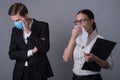 Portrait of two young businessmen in business clothes. The masked guy covers his face with his hand, fearing infection by a sick