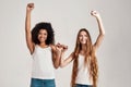 Portrait of two young diverse women, best friends smiling at camera while raising arm and making a pinkie promise sign