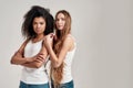 Portrait of two young diverse women wearing white shirts looking at camera while posing together isolated over grey Royalty Free Stock Photo