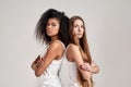 Portrait of two young diverse women wearing white shirts looking at camera while standing back to back isolated over Royalty Free Stock Photo