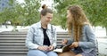 A portrait of two young girls sitting on a bench and looking at a book, discussing something, laughing, smiling, marking