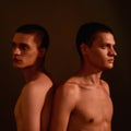 Portrait of two young half naked men, caucasian twin brothers standing back to back  over brown background in Royalty Free Stock Photo