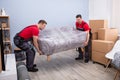 Male Movers Carrying Wrapped Sofa In New House Royalty Free Stock Photo