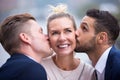 Two young men kissing woman on her cheeks