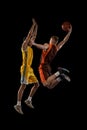 Portrait of two young men, professional basketball players in a jump, throwing ball into basket isolated over black Royalty Free Stock Photo