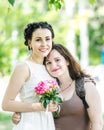 Portrait of two young pretty women hugging each other in green summer park. Pretty females bride with bouquet of roses and her fri Royalty Free Stock Photo