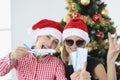 Portrait of two young women in santa claus hats holding airplane and tickets against of New Year tree