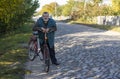Ukrainian senior peasant standing with ancient bicycle on an ancien cobblestone road