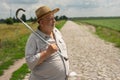 Portrait of Ukrainian senior farmer in straw hat standing on cobblestone road and taking walking stick