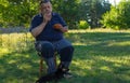 Portrait of Ukrainian senior man sitting in summer garden with cap of tea while his little puppy sitting near master feet Royalty Free Stock Photo