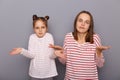 Portrait of uncertain woman and little girl with hair buns wearing casual clothes standing isolated over gray background, family Royalty Free Stock Photo