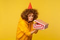 Portrait of unhappy displeased curly-haired woman with funny party cone hat holding opened gift box Royalty Free Stock Photo