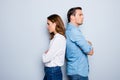 Portrait of unhappy frustrated couple standing back to back not speaking to each other after an argument while standing on grey ba