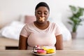 Portrait of unhappy overweight black woman with adhesive bandage on her mouth sitting at table with plate of sweets