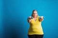 Portrait of an unhappy overweight woman with dumbbells in studio on a blue background. Royalty Free Stock Photo