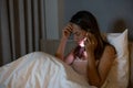 Portrait unhappy young Asian woman talking on mobile phone on bed at night looking down. Human face expression, bad news reaction Royalty Free Stock Photo