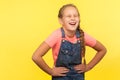 Portrait of unhealthy child with braid in denim overalls clutching belly, feeling discomfort or pain in stomach