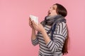 Portrait of unhealthy woman wrapped in warm scarf sneezing in napkin, suffering allergy or flu symptoms