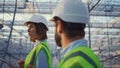 Portrait uniform engineers talking in empty glasshouse analysing manufacture.