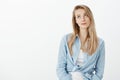 Portrait of unimpressed beautiful european woman with blond hair, smirking and looking upwards with indifferent