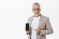 Portrait of unimpressed unsure and hesitant elegant wealthy mature businessman in glasses and suit holding smartphone