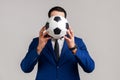 Portrait of unknown anonymous businessman supporting favorite team covering face with soccer ball.