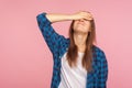 Portrait of unlucky girl in checkered shirt standing with facepalm gesture, feeling regret and sorrow, blaming herself