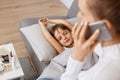 Portrait of unrecognizable mother calling a doctor because of her daughters illness, child lying on sofa on pillow under blanket, Royalty Free Stock Photo