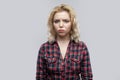 Portrait of unsatisfied beautiful blonde young woman in casual red checkered shirt standing and looking at camera with sad eyes