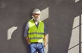 Mature builder or construction engineer in uniform and hard hat standing by grey house wall Royalty Free Stock Photo