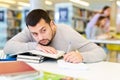 Portrait of upset adult man with stack of books on table in room of public library