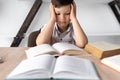 portrait of upset boy with textbooks and headache. Schoolboy at a desk with open books in the library. Student stress