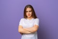 Portrait of upset brunette woman in white casual t shirt standing with arms folded over purple background. Attractive young woman Royalty Free Stock Photo
