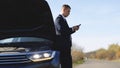 Portrait of upset businessman staying on countryside road, using smartphone for calling help evacuator evacuating repair