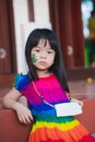 Portrait upset child leaning against wooden battens look at camera. Girl wear colorful dress.