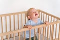 Portrait of upset crying baby standing in crib getting hysterical seeking attention of parents