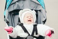 Portrait of upset crying Caucasian baby girl outside. Screaming child toddler in white warm clothes sitting lying in a stroller Royalty Free Stock Photo