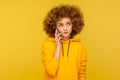 Portrait of upset curly-haired woman in urban style hoodie calling friend, talking on smartphone with serious expression