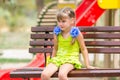 Portrait of upset five year old girl who is sitting on the bench on the background of the playground Royalty Free Stock Photo