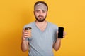 Portrait of upset handsome bearded young hipster man in gray t shirt and blindfold standing with coffee in one hand and phone with Royalty Free Stock Photo