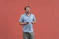 Portrait of an upset hipster man showing credit card standing over red background, holding mobile phone. Confused boy using online Royalty Free Stock Photo