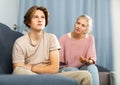 Upset and offended teenager sitting on sofa while mother soothing him