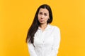 Portrait of upset offended young woman in white casual shirt standing and looking camera isolated on bright yellow