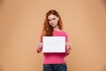 Portrait of an upset pretty redhead girl showing blank board