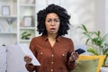 Portrait of upset and shocked African American young woman checking financial accounts and credit. He is holding a phone Royalty Free Stock Photo