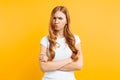 Portrait of an upset young girl standing with folded arms and offended face, on yellow background Royalty Free Stock Photo