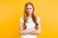 Portrait of an upset young girl standing with folded arms and offended face, on yellow background Royalty Free Stock Photo