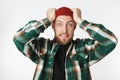 Portrait of uptight man wearing hat and plaid shirt screaming and grabbing head, while standing isolated over white background