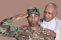 Portrait of US Marine Corps soldier with father saluting over brown background